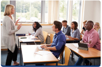 Photograph of a classroom setting with a teacher standing and speaking to a group of adult students seated at desks
