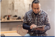 Photograph of a person wearing a plaid shirt and long sleeves using a tablet while seated indoors - original