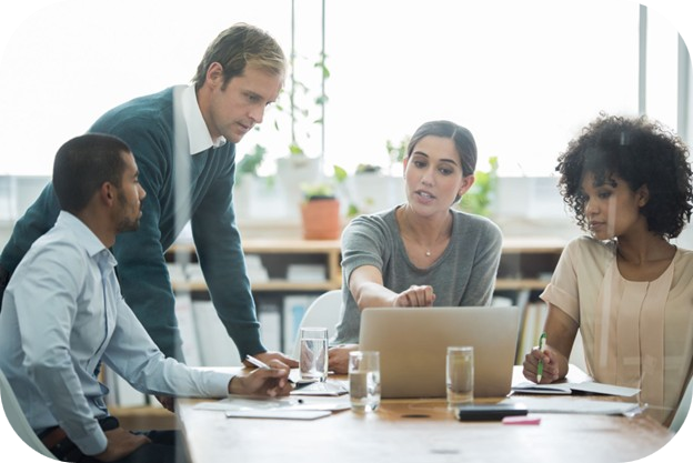 Photograph of four professionals engaged in a collaborative meeting around a table with laptops, notebooks, and glasses of water rounded corners