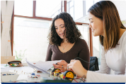 Photograph of two women working together on an electronics project in a bright room with large windows - original