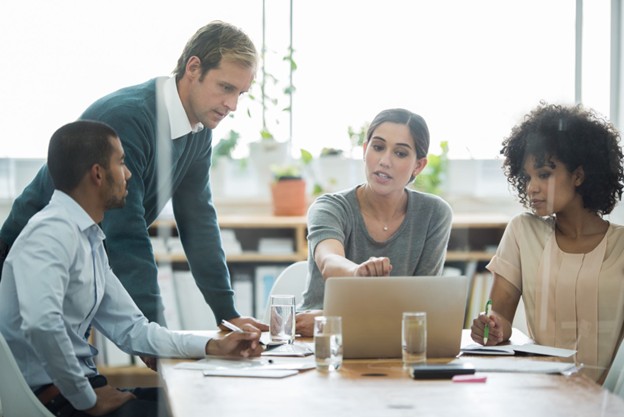 Four diverse colleagues collaborating around a table with a laptop
