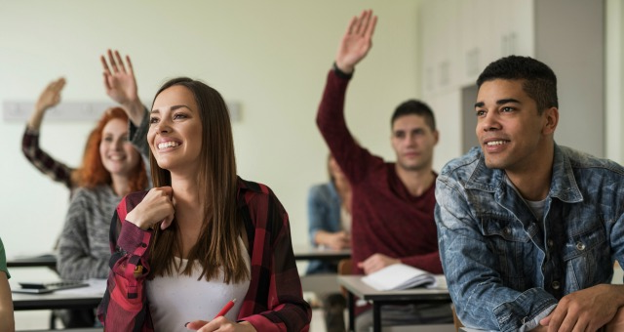 Photograph of a classroom setting with students engaged in a lesson, some raising their hands to participate. 